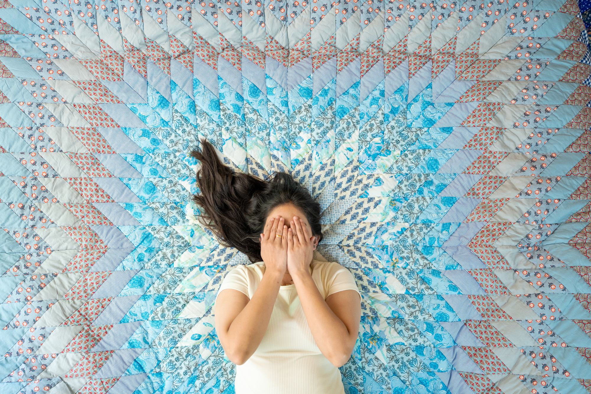 A woman lying on a hand-quilted star patchwork quilt, her hair fanned across the stitching