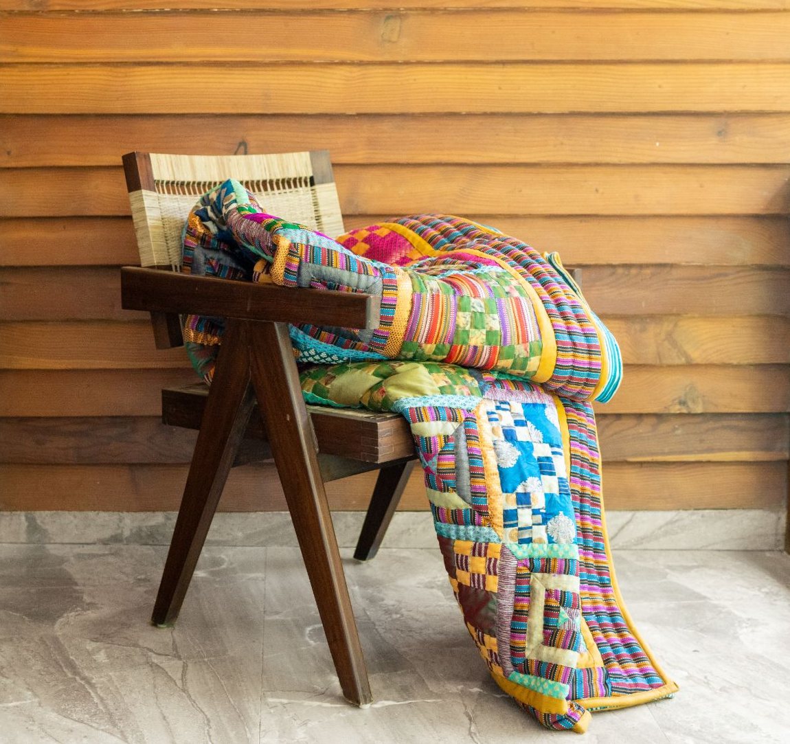 A patchwork quilt draped over a cane chair on a wooden veranda