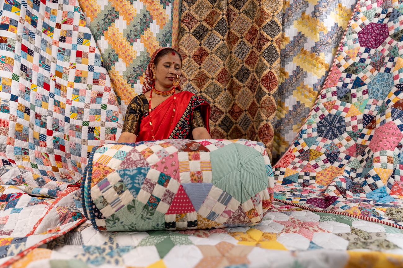 A Purkal Didi in a red saree surrounded by patchwork quilts