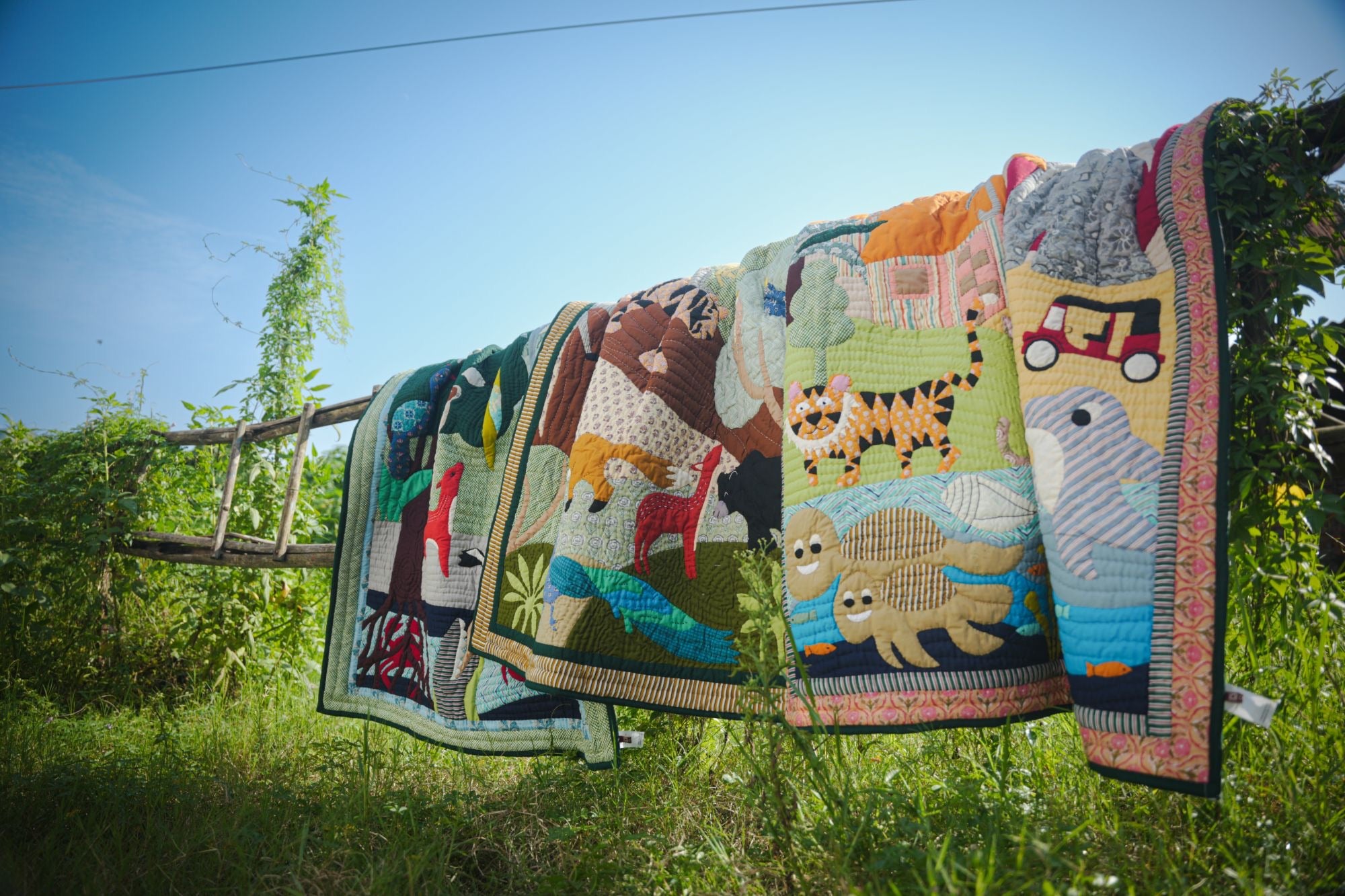 Hand-appliquéd art quilts of monkeys, birds, a peacock, a deer, tigers and an elephant, hung outdoors in the sun