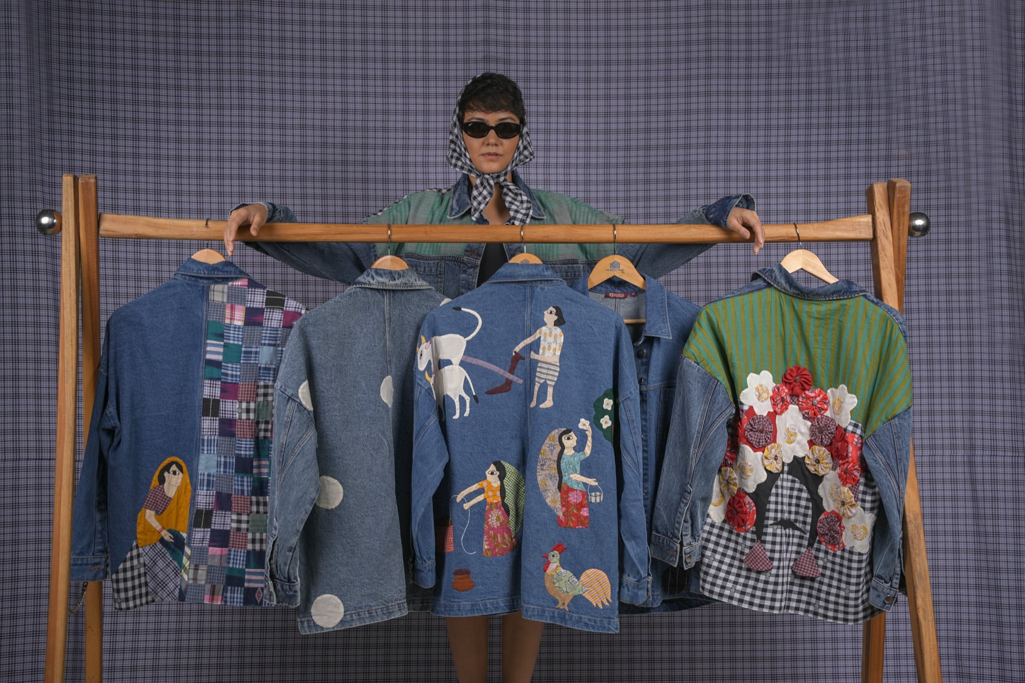 A woman in a patchwork denim jacket and headscarf in front of a rail of appliquéd jackets